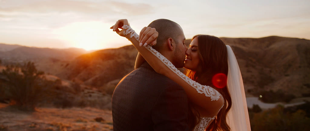 Edmond and Lauren kissing at sunset above the hills, her arm draped over his shoulder